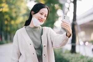 Asiatin nimmt ihre Gesichtsmaske ab, um ihr Telefon zu benutzen foto