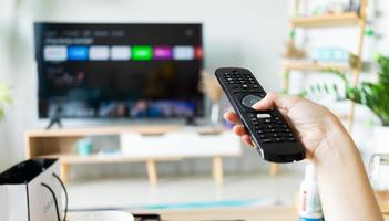 asiatische frau, die fernsehfernbedienung in der hand hält, um den kanal zu wechseln foto