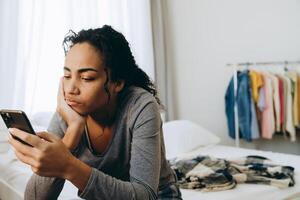 junge schwarze Frau mit Handy beim Sitzen auf dem Bett foto