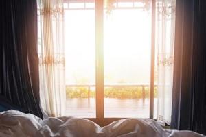 Fensteransicht Natur grüner Berg im Bett am Schlafzimmermorgen und Sonnenlicht - Fensterglas mit Vorhängen foto