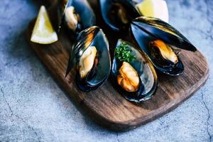 gekochte Muscheln mit Kräuterzitrone und dunklem Plattenhintergrund - frische Meeresfrüchte auf Holzbrett im Restaurant Muschelschalenessen foto