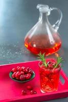 Glas frischer Cranberry-Fruchtsaft mit Rosmarin und sasischer Obstschale in einem roten Tablett, Krug, auf einem grauen Schieferhintergrund