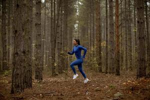 junge Frau, die im Herbst auf dem Waldweg läuft foto