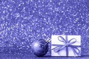 Geschenkbox und Weihnachtskugel auf glänzendem Goldgrund. Trendfarbe des Jahres 2022