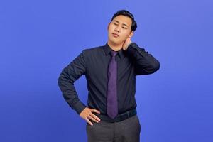 Gut aussehender junger Geschäftsmann, der sich nach einem langen Arbeitstag auf violettem Hintergrund müde fühlt foto