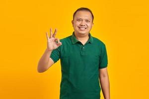 Porträt eines lächelnden jungen asiatischen Mannes, der mit den Fingerhänden ein okayzeichen auf gelbem Hintergrund macht foto