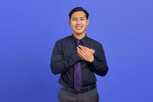 Foto eines lächelnden gutaussehenden Geschäftsmannes, der beide Handflächen auf der Brust auf violettem Hintergrund hält