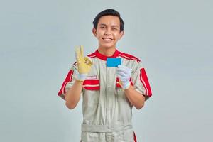 Porträt eines gutaussehenden jungen Mechanikers, der Kreditkarte in der Hand zeigt und ein OK-Zeichen mit lächelndem Ausdruck auf grauem Hintergrund zeigt foto