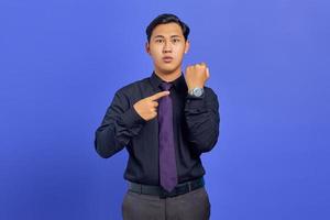 hübscher junger Geschäftsmann, der die Zeit auf der Armbanduhr auf violettem Hintergrund überprüft foto