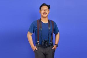 fröhlicher und aufgeregter hübscher Fotograf, der eine professionelle Kamera auf violettem Hintergrund hält foto
