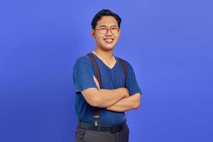 Porträt eines lächelnden jungen asiatischen Mannes, der seine Arme verschränkt und eine Brille auf violettem Hintergrund trägt