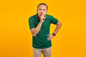 attraktiver junger asiatischer mann finger auf den lippen und macht eine stille geste auf gelbem hintergrund foto