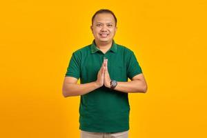 Porträt eines lächelnden asiatischen jungen Mannes, der Hände hält und über gelbem Hintergrund fleht foto