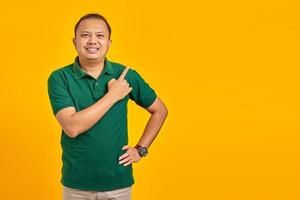Porträt eines lächelnden jungen asiatischen Mannes, der mit dem Finger auf den Kopierraum auf gelbem Hintergrund zeigt