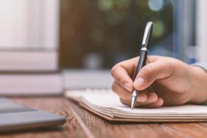 Frau mit Stift sitzt auf einem Schreibtisch und schreibt foto