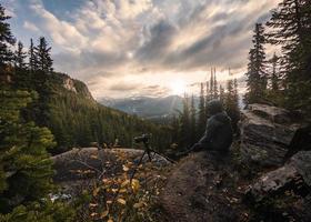 Mann Fotograf sitzt mit Besichtigung des Sonnenaufgangs auf einer Klippe im Lake Louise foto