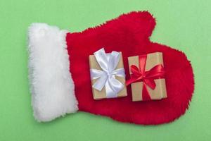 Weihnachtskomposition roter Pelzhandschuh von Santa Claus mit Geschenken auf grünem Hintergrund. Vorlage für Postkarten, Verpackungen foto