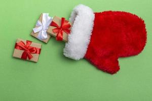 Weihnachtskomposition roter Handschuh von Santa Claus mit Geschenken auf grünem Hintergrund. Vorlage für Postkarten, Verpackungen foto