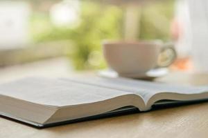 Offene Bibel mit weißer Tasse Kaffee mit der Morgenatmosphäre auf einem Holztisch in der Nähe der Fensterbank foto