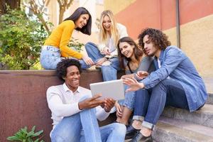 multiethnische Gruppe junger Menschen, die im Freien im städtischen Hintergrund ein digitales Tablet betrachten.