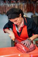 Frau schneidet frisches Fleisch in einer Metzgerei mit Metallsicherheitsnetzhandschuh foto