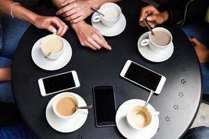 Hände mit Kaffeetassen und Smartphones in einem städtischen Café.