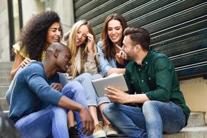 multiethnische Gruppe junger Menschen, die auf einen Tablet-Computer schauen foto