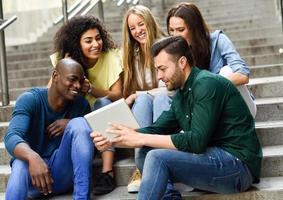 multiethnische Gruppe junger Menschen, die auf einen Tablet-Computer schauen foto