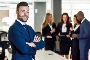 Geschäftsmannführer in einem modernen Büro mit Geschäftsleuten, die im Hintergrund arbeiten foto