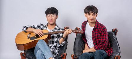 Zwei junge Männer saßen auf einem Stuhl und spielten Gitarre. foto