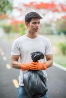 Ein Mann mit orangefarbenen Handschuhen sammelt Müll in einer schwarzen Tasche. foto