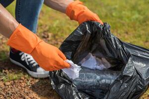 Ein Mann mit orangefarbenen Handschuhen sammelt Müll in einer schwarzen Tasche. foto