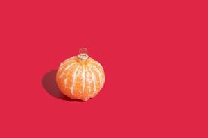 Mandarine in Form eines Weihnachtsbaumspielzeugs auf rotem Grund mit Kopierraum. minimalistisches Weihnachtskonzept foto