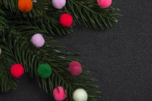 Weihnachtskarte. Flatley Zweige eines Weihnachtsbaumes bunte Pelzspielzeuge auf schwarzem Hintergrund. foto