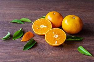 frische Orangenfrüchte und Orangenfrüchte halbiert auf einem Holztisch