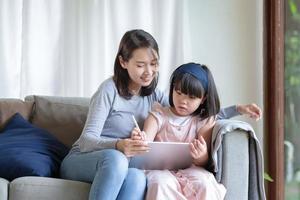 Asiatische Mutter, die ihrer süßen Tochter das Lernen im Wohnzimmer beibringt foto