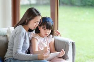 glückliche asiatische Mutter, die ihrer süßen kleinen Tochter das Lernen im Wohnzimmer zu Hause beibringt