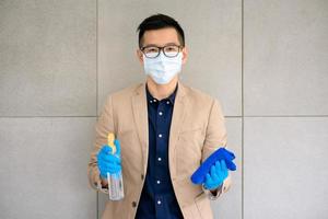 Geschäftsmann, der Maske trägt und persönliche Desinfektionsmittel verwendet, um sein Büro zu reinigen, um die Hygiene zu wahren. Präventiv während der Epidemie durch Coronavirus oder Covid19.