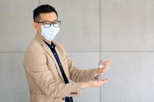 Geschäftsmann, der eine Maske trägt und ein persönliches Desinfektionsmittel verwendet, um seine Hand im Büro zu reinigen, um die Hygiene zu wahren. Während der Epidemie durch Coronavirus oder Covid19 vorbeugend.