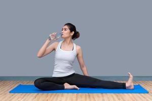 Junge asiatische Frau trinkt Wasser nach dem Training im gesunden Sportstudio. Fotokonzept für Yoga-Sport und gesunden Lebensstil