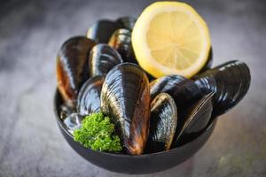 Rohe Muscheln mit Kräuterzitrone auf Schüssel und dunklem Hintergrund - frische Meeresfrüchte auf Eis im Restaurant oder zum Verkauf auf dem Markt Muschelschalenessen