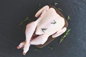 frisches rohes Huhn ganz auf schwarzem Plattenhintergrund Rosmarin-Hühnerfleisch-Holzschneidebrett foto