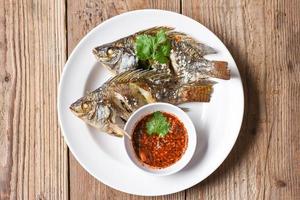 gekochtes Essen gegrillter Tilapia-Fisch - Tilapia-Süßwasserfisch auf weißem Teller mit Chilisauce foto