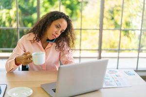 lateinische frau, die mit kaffeetasse am arbeitsplatz arbeitet foto