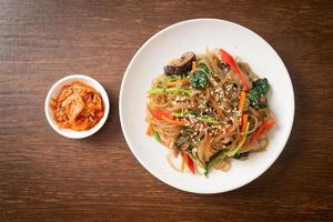 Japchae oder gebratene koreanische Fadennudeln mit Gemüse und Schweinefleisch, garniert mit weißem Sesam foto