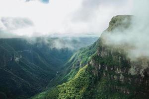 fortaleza canyon mit steilen felsigen klippen bedeckt von dichtem wald und nebel, der die schlucht in der nähe von cambara do sul heraufzieht. eine kleine landstadt im süden brasiliens mit erstaunlichen natürlichen touristenattraktionen. foto