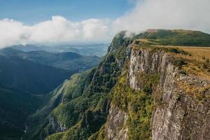 fortaleza canyon mit steilen felsigen klippen bedeckt von dichtem wald und nebel, der die schlucht in der nähe von cambara do sul heraufzieht. eine kleine landstadt im süden brasiliens mit erstaunlichen natürlichen touristenattraktionen. foto