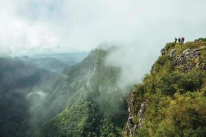 Menschen auf steilen Felsklippen in der Fortaleza-Schlucht, bedeckt von Wald und Nebel, der aus dem Tal in der Nähe von Cambara do Sul aufsteigt. eine kleine ländliche stadt im süden brasiliens mit erstaunlichen natürlichen touristenattraktionen. foto