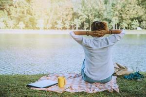 Frauen sitzen eine entspannte Flussseite im Park. sitzend mit einem Notebook arbeiten und Kaffee trinken. im Urlaub foto