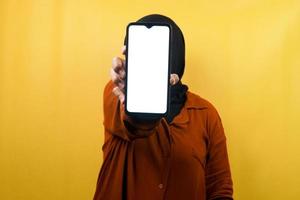 schöne junge asiatische muslimische frau, die ein smartphone mit weißem oder leerem bildschirm hält, app fördert, etwas fördert, isoliert, werbekonzept